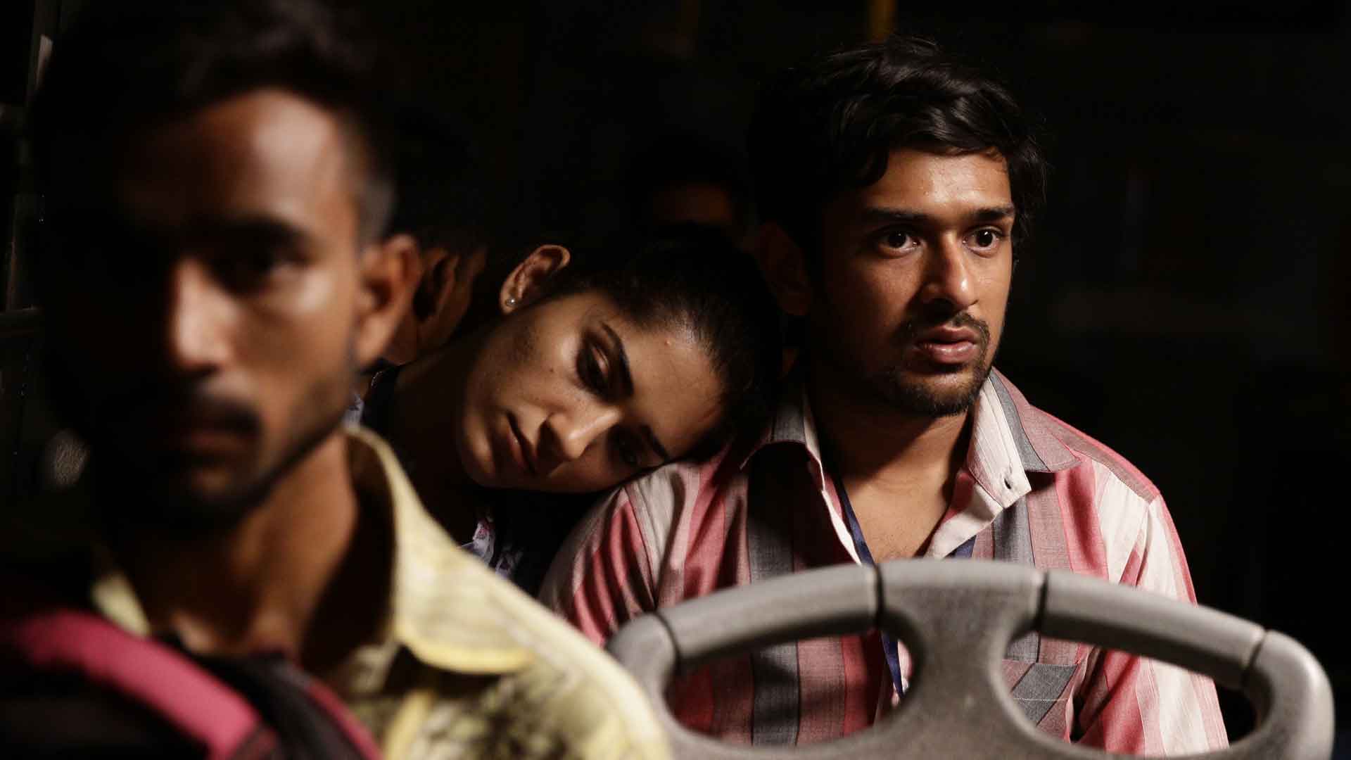 Still image from "Agra," directed by Kanu Behl. A young South Asian man looks nervous while riding in a vehicle with a woman resting her head on his shoulder. A blurred driver is to the far left.