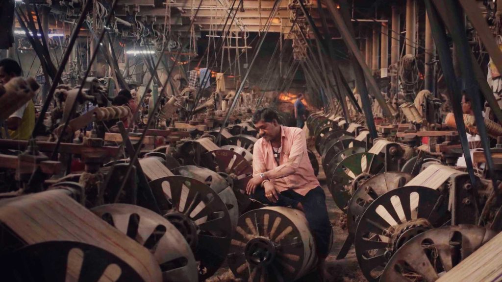 A man works on a machine in a vast jute processing factory in West Bengal, India. Still from the documentary, "The Golden Thread"