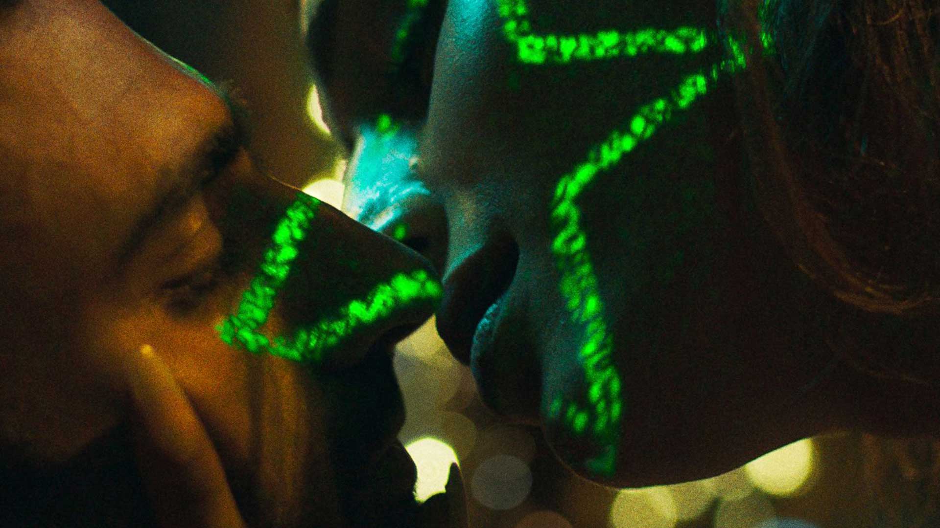 A closeup of two people kissing in the dark, with the bright light of a projection in the shape of a star hitting their faces.