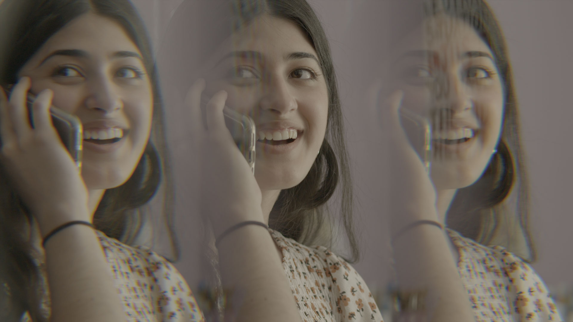 Image from film "TikTok, Boom," showing a triple-reflected image of a young smiling South Asian woman talking on a cellphone