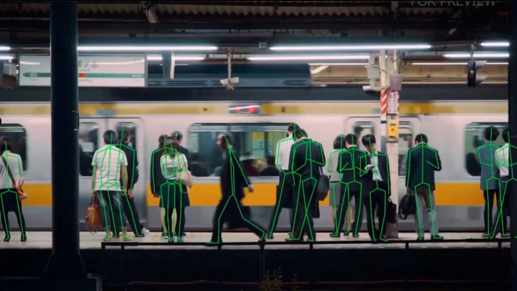 a straight-on view, as if from another train, of people gathering on a subway platform. Their gestures are outlined with simple skeletal frames, machine-like, drawn in vivid green lines on their bodies.