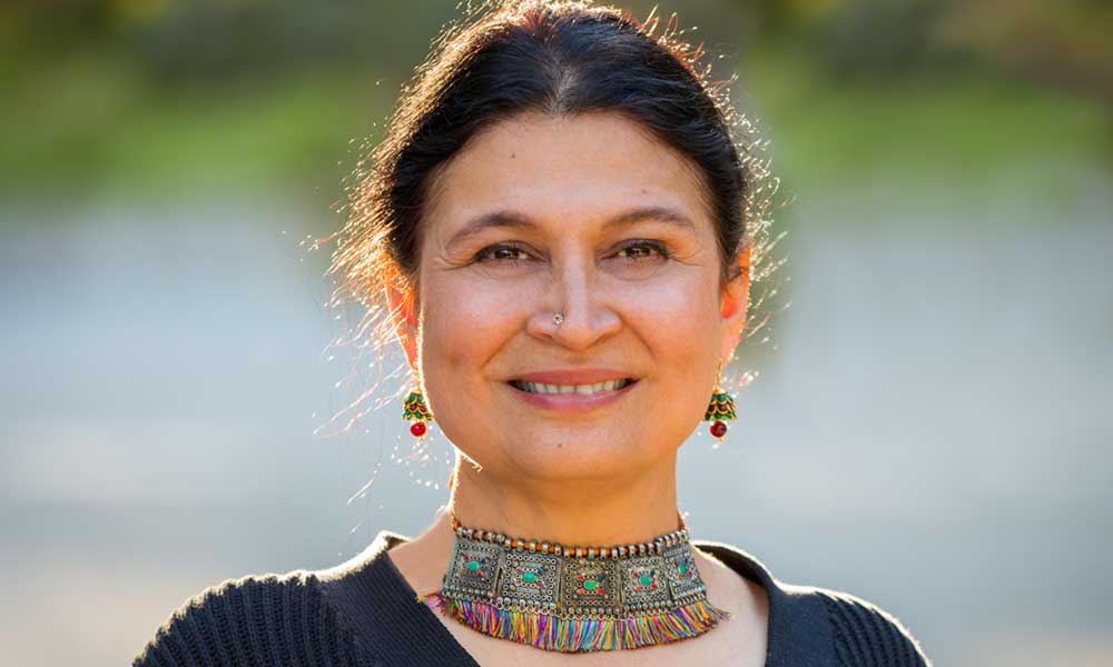 Color portrait of filmmaker Alka Raghuram outdoors. She wears a dramatic necklace and looks put-together but natural.