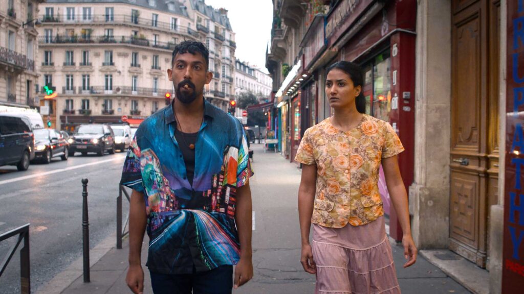 Still from The Loyal Man, directed by Lawrence Valin: a young man and woman of Indian heritage walking in the streets of Paris, about a foot of space between them. The man looks cocky and tough; the woman looks concerned.