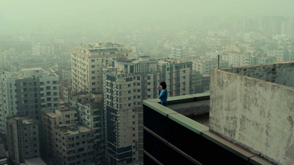 Still from Sand City. A woman viewed from above looks out over a vast array of buildings enveloped in fog or smog.