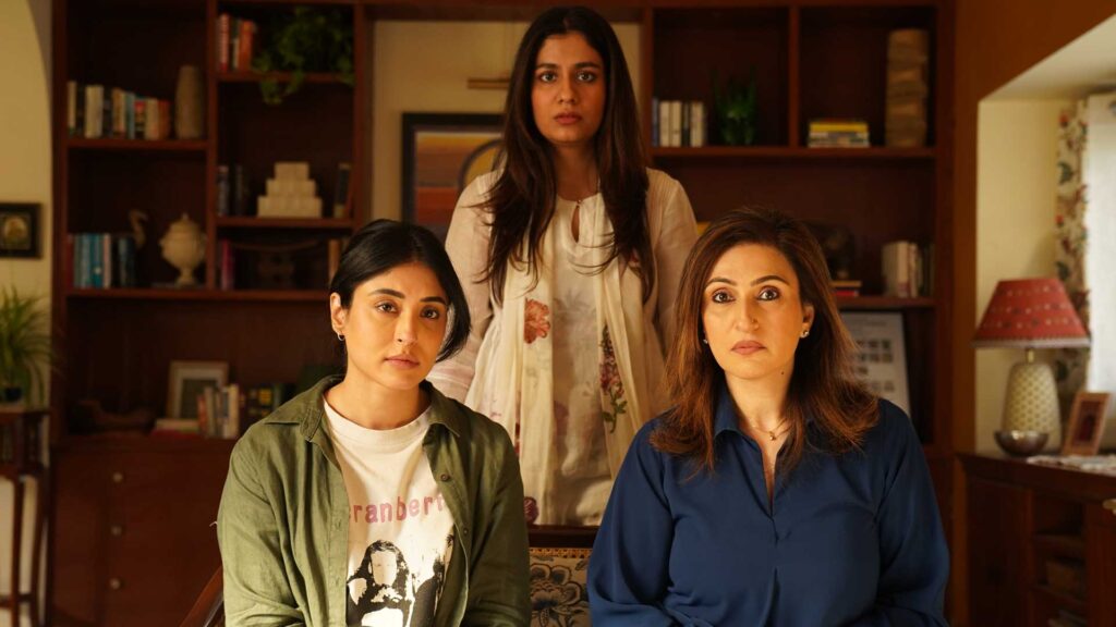 Still from The Great Shamsuddin Family. Three women of different ages who appear to be related and are in a living-room setting look directly at the camera.